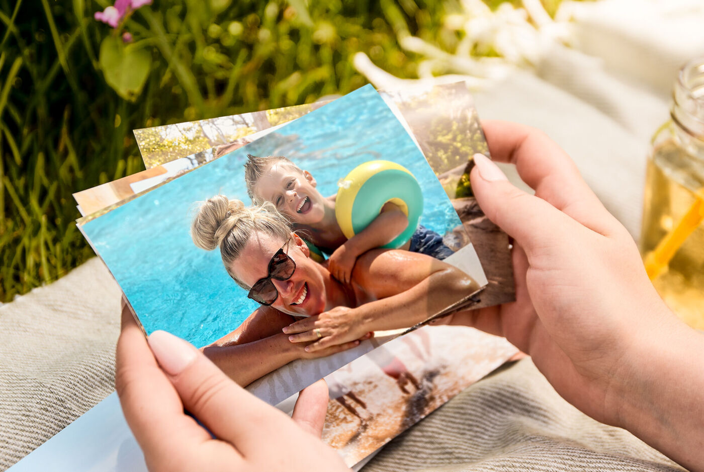 Hände halten einen Stapel Fotos, obenauf ein Bild von zwei lachenden Personen im Pool.