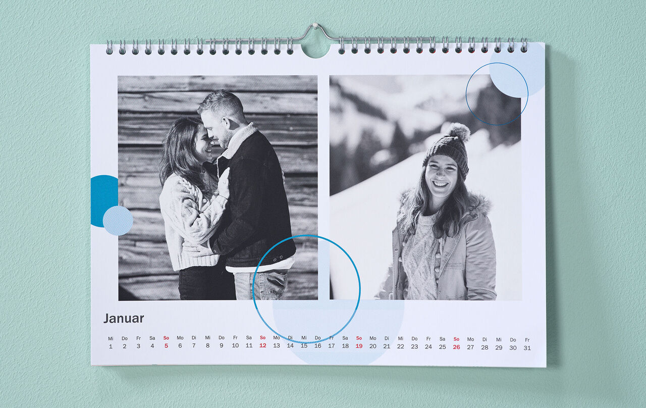 Kalender mit winterlichen Schwarz-Weiss-Fotos und kreisförmigen Cliparts in Blau hängt an einer mintgrünen Wand.