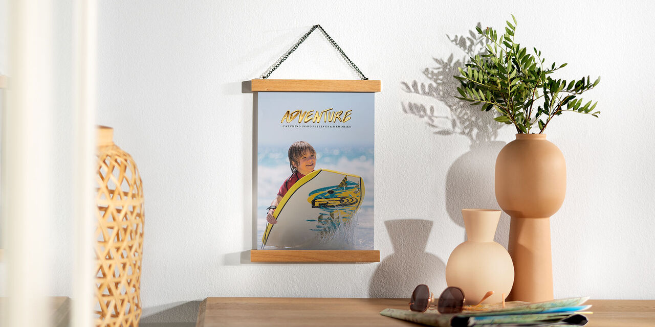 Questo poster mostra un bambino sulla spiaggia. Guarda verso la telecamera e tiene in mano una tavola da surf. Sullo sfondo si vede il mare e le sue onde. In alto si vede il cielo azzurro.