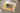 Un FOTOLIBRO CEWE chiuso si trova su un divano accanto a un peluche e a una coperta. La copertina del libro mostra una foto di tre bambini piccoli sdraiati su un prato che sorridono alla macchina fotografica. Il titolo recita «Per la nonna». Una macchia gialla ad acquerello ed elementi floreali fanno da sfondo al frontespizio.